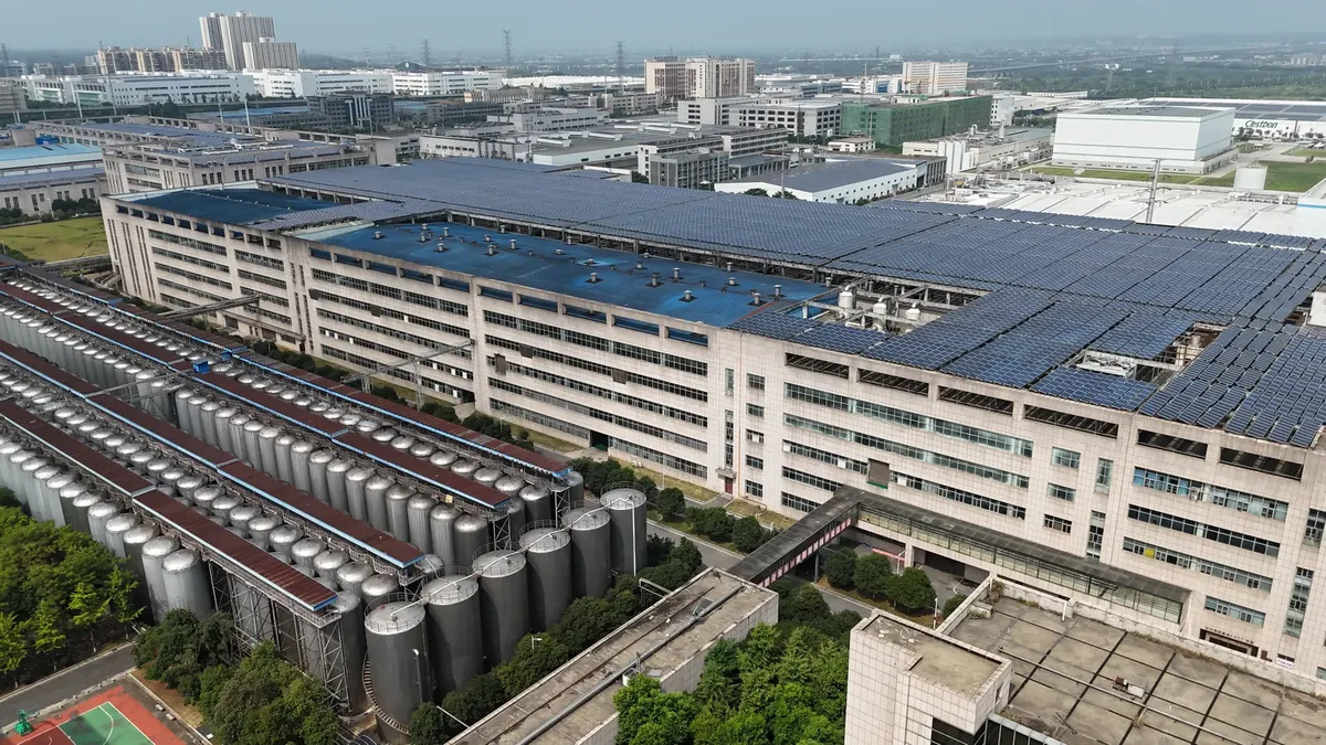 現代的な工業ビルの空撮写像で、太陽光発電パネルと貯蔵タンクが見える。