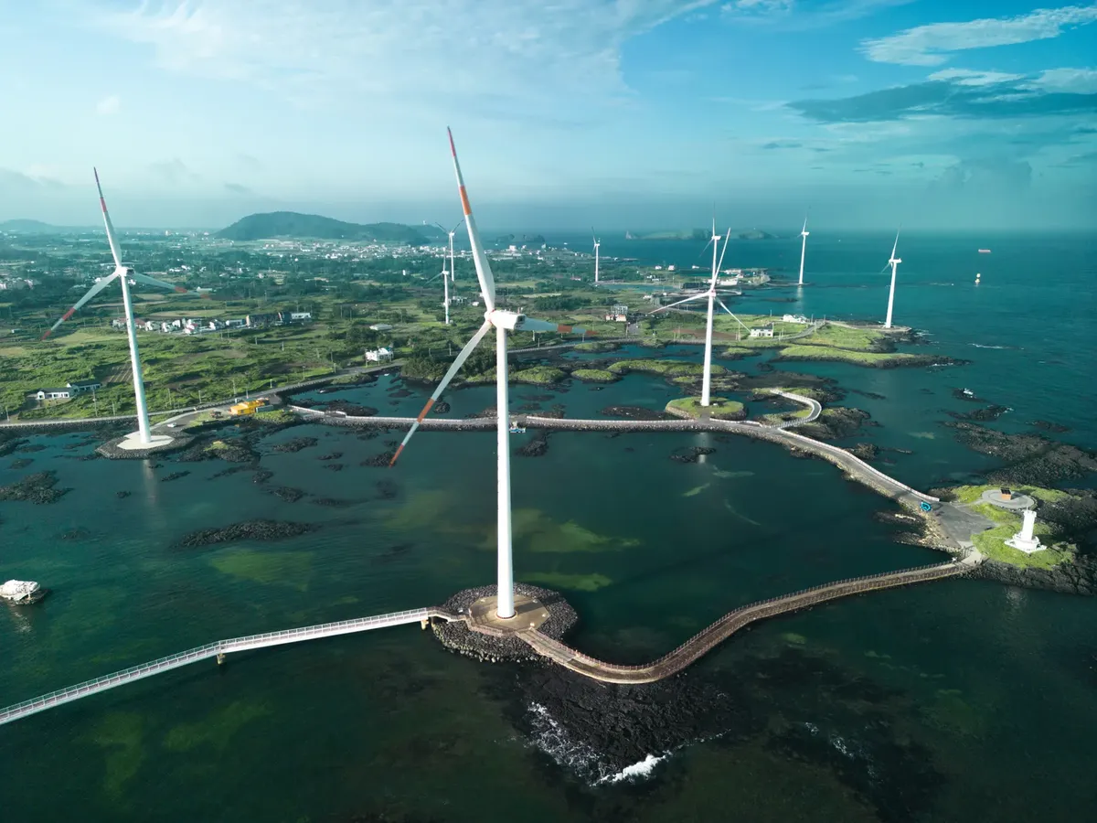 Aerial photo of wind turbines set against a coastal landscape with bright blue waters.
