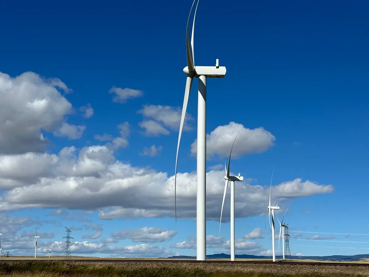 Wind turbines in open landscape with blue sky and clouds, emphasizing renewable energy.
