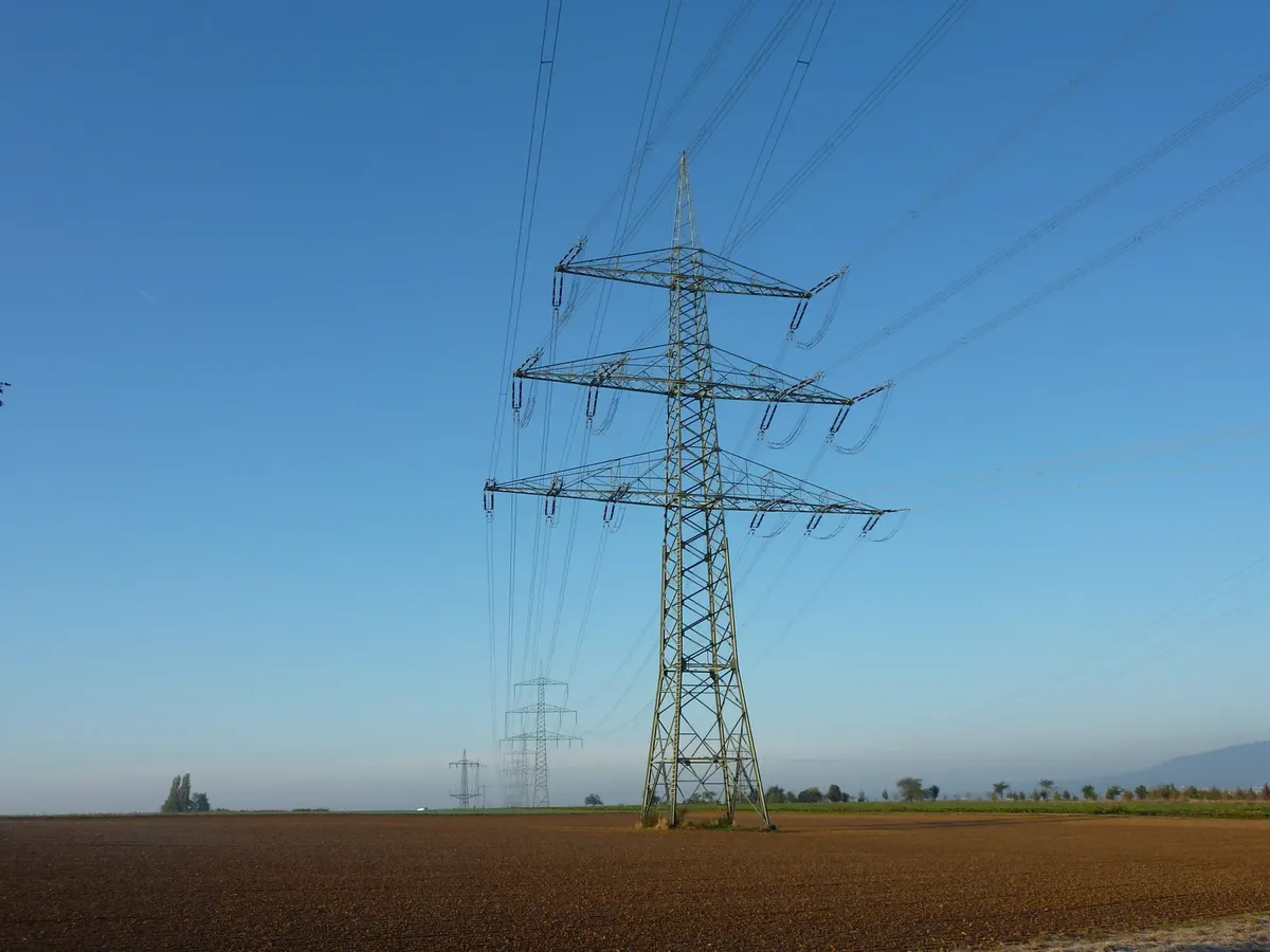 高い電圧の電線が塔に立っているオープンフィールドにあり、青い空の下に見える。