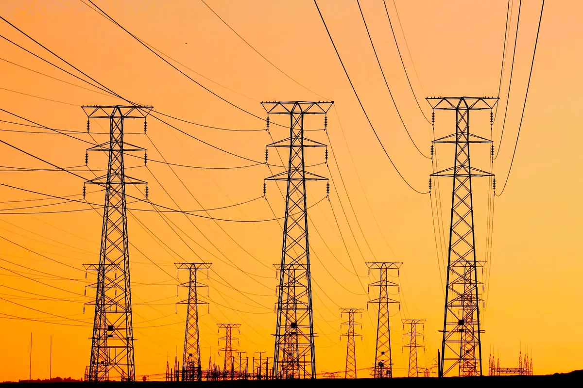 夕方の鮮やかなオレンジな夕焼けの背景に、影が見える電線、エネルギーとインフラを象徴している。