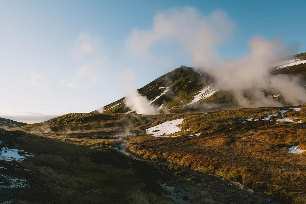 Explore a breathtaking geothermal landscape with steam rising amid snow-capped mountains.