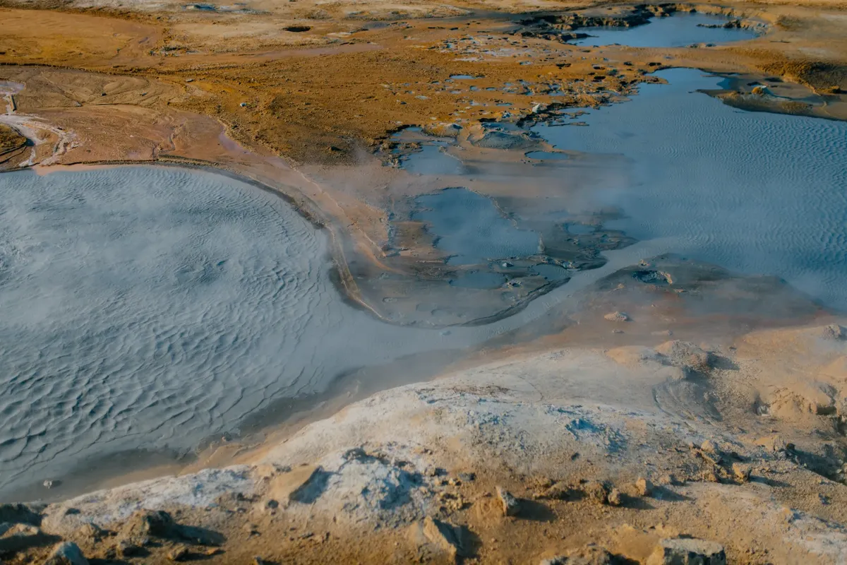 Aerial view of Icelandic geothermal landscape featuring barren terrain and steaming hot springs.
