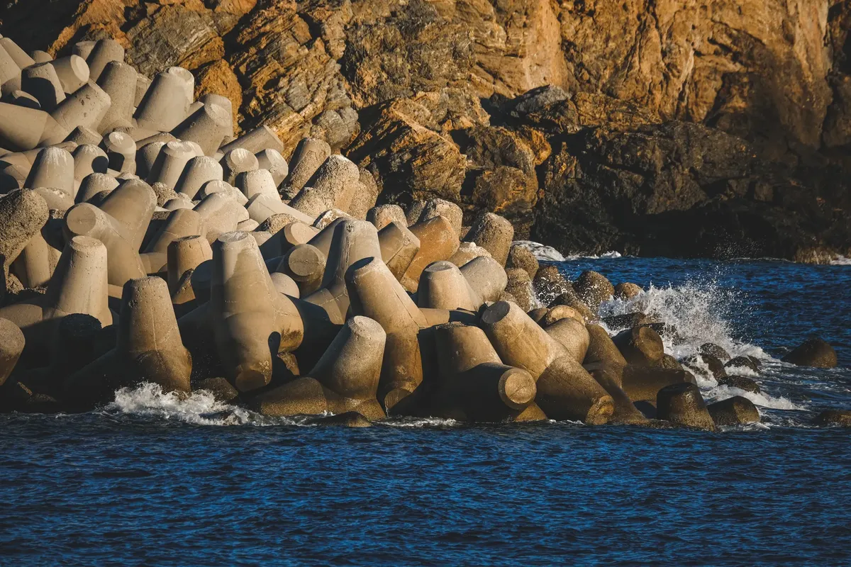 Concrete breakwater structures meet ocean waves against a rocky coastline.